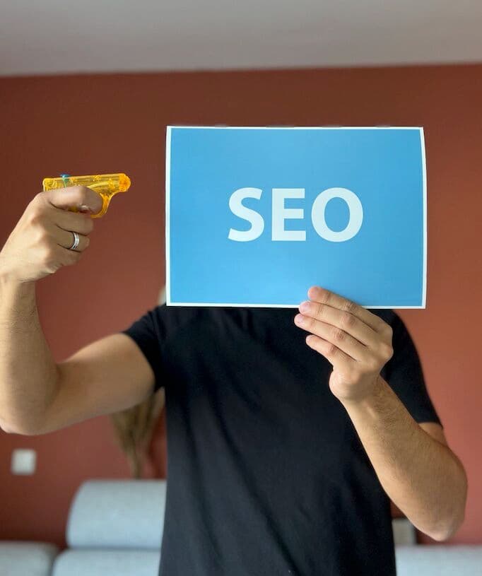 man houdt waterpistool tegen tekst SEO aan en geeft daarmee het idee dat SEO dood is